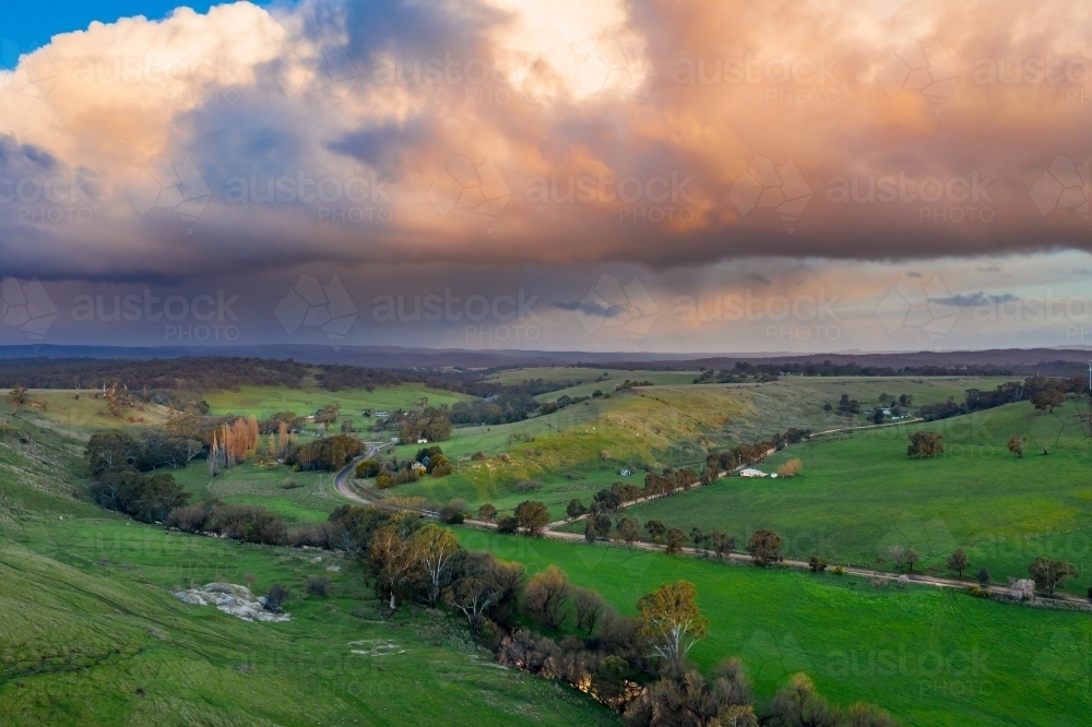 Rain falling from colored storm clouds over green rural countryside - Australian Stock Image