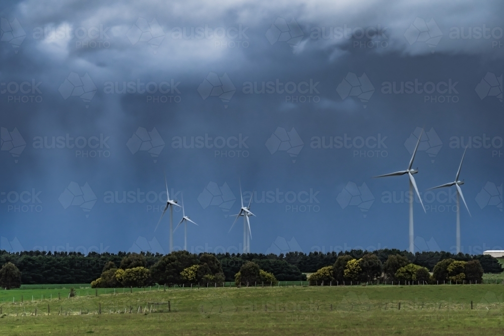 Rain falling from dark stormy skies hovering over tall wind turbines - Australian Stock Image