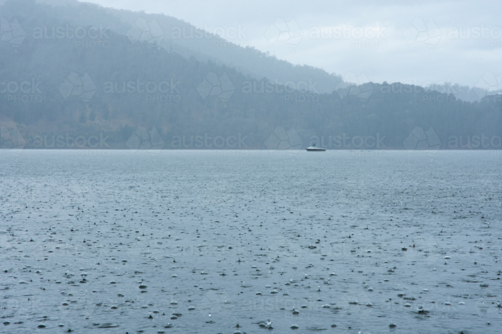 Rain on lake with boat and hills in distance - Australian Stock Image