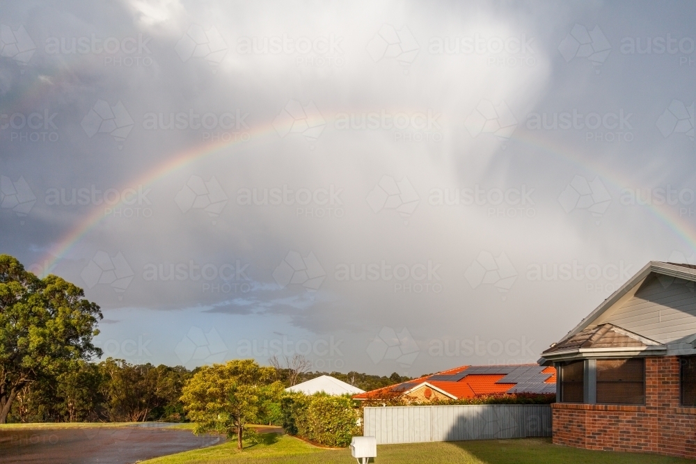 rainbow arcing over homes at the end of the street. - Australian Stock Image