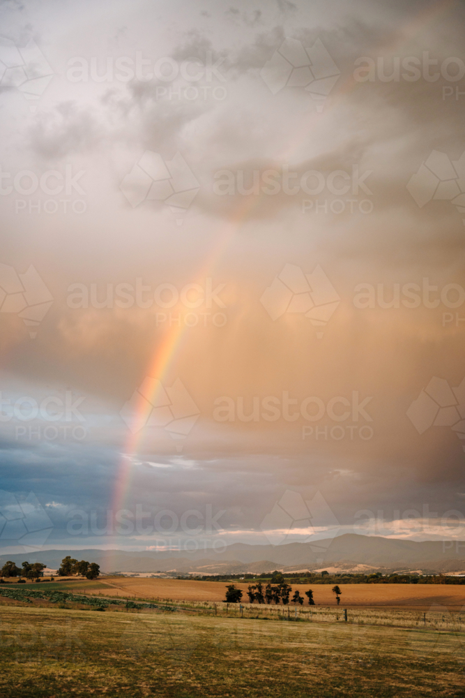Rainbow descending through rain showers above rolling rural farmland - Australian Stock Image