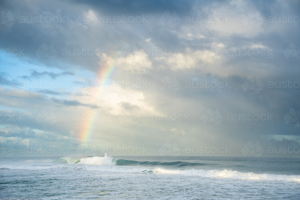 Rainbow forming over crashing ocean waves at Scarborough Beach, Perth, Western Australia - Australian Stock Image