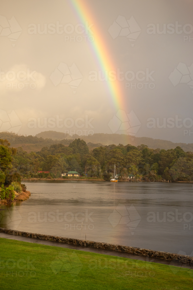 Rainbow over harbour waters with yacht on calm waters - Australian Stock Image