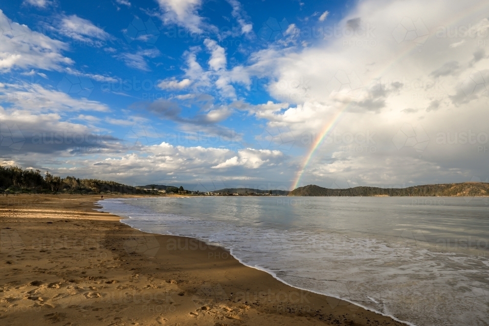 Rainbow over ocean and sandy beach - Australian Stock Image