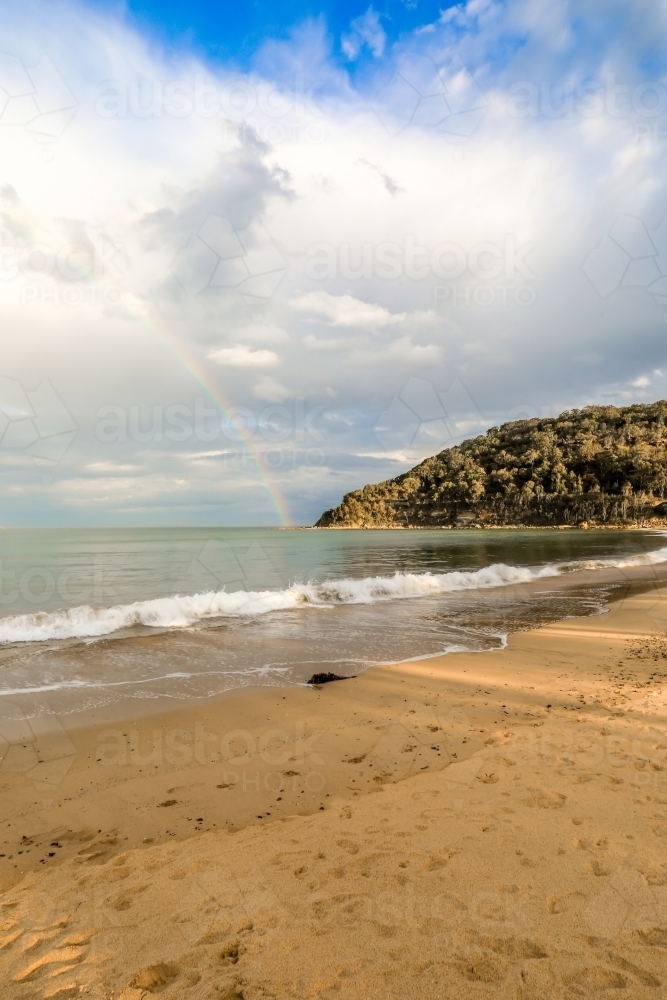 Rainbow over ocean and sandy beach - Australian Stock Image