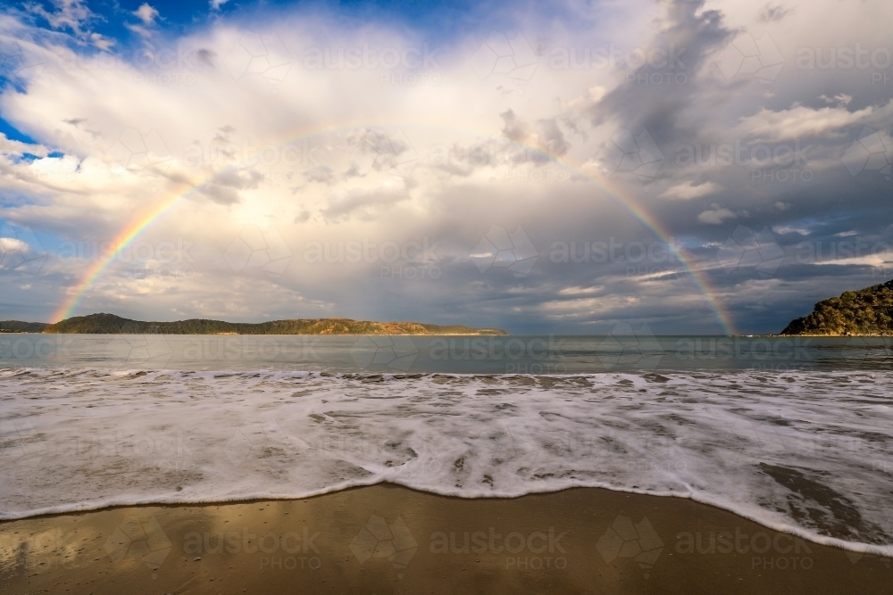 Rainbow over ocean and sandy beach - Australian Stock Image