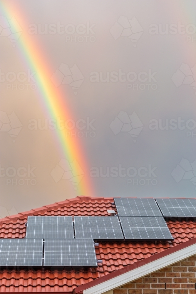 Rainbow over roof of house with solar panels shining after rain storm - Australian Stock Image