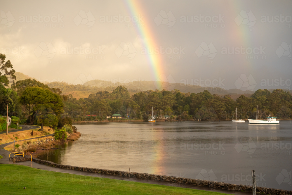 Rainbows over harbour waters with yacht on calm waters - Australian Stock Image