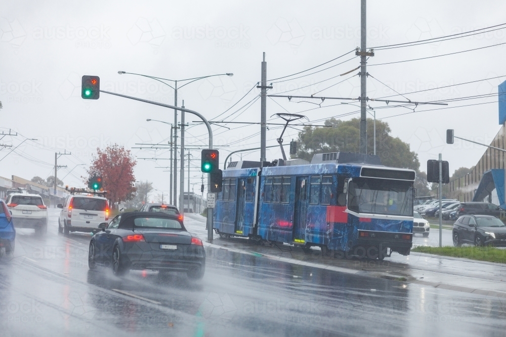rainy day traveling in city with cars and tram at intersection - Australian Stock Image