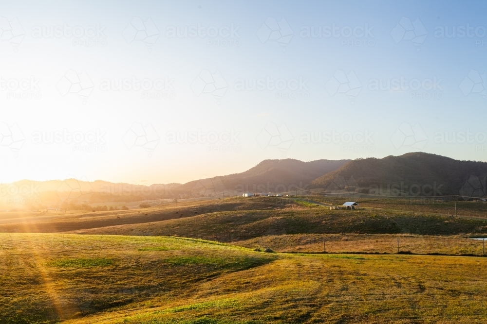 Ray of sunlight over green hills of farm in lush countryside - Australian Stock Image