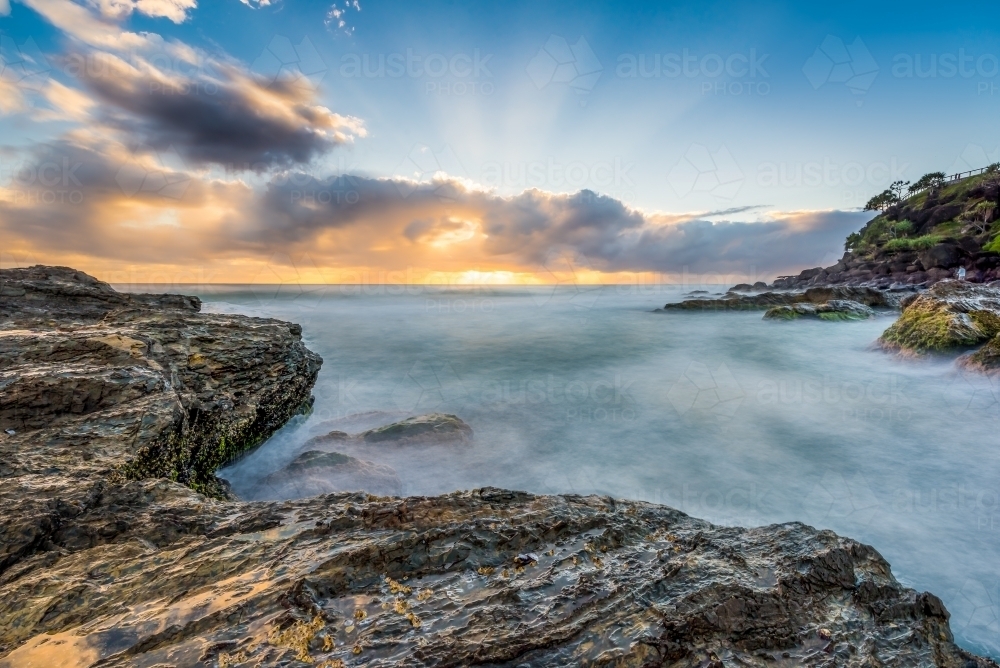 Rays of sunshine from behind clouds over ocean waves - Australian Stock Image