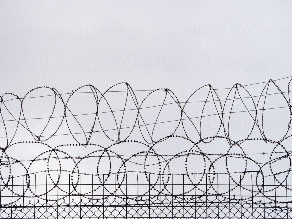 Razor wire on top of a fence against a grey sky - Australian Stock Image