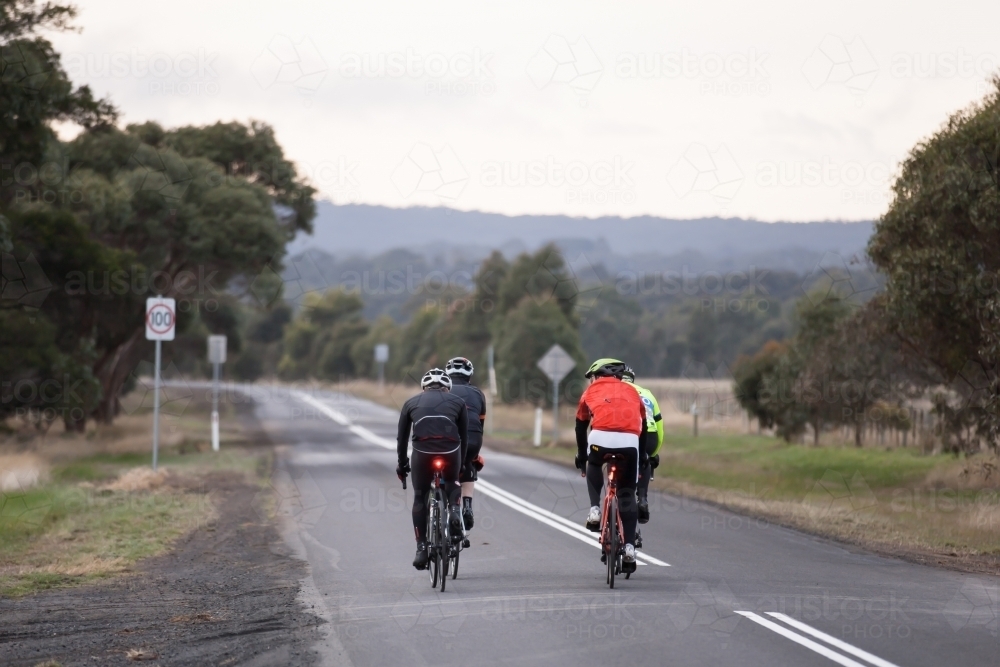 Rear view of cyclists riding on a country road in early morning - Australian Stock Image