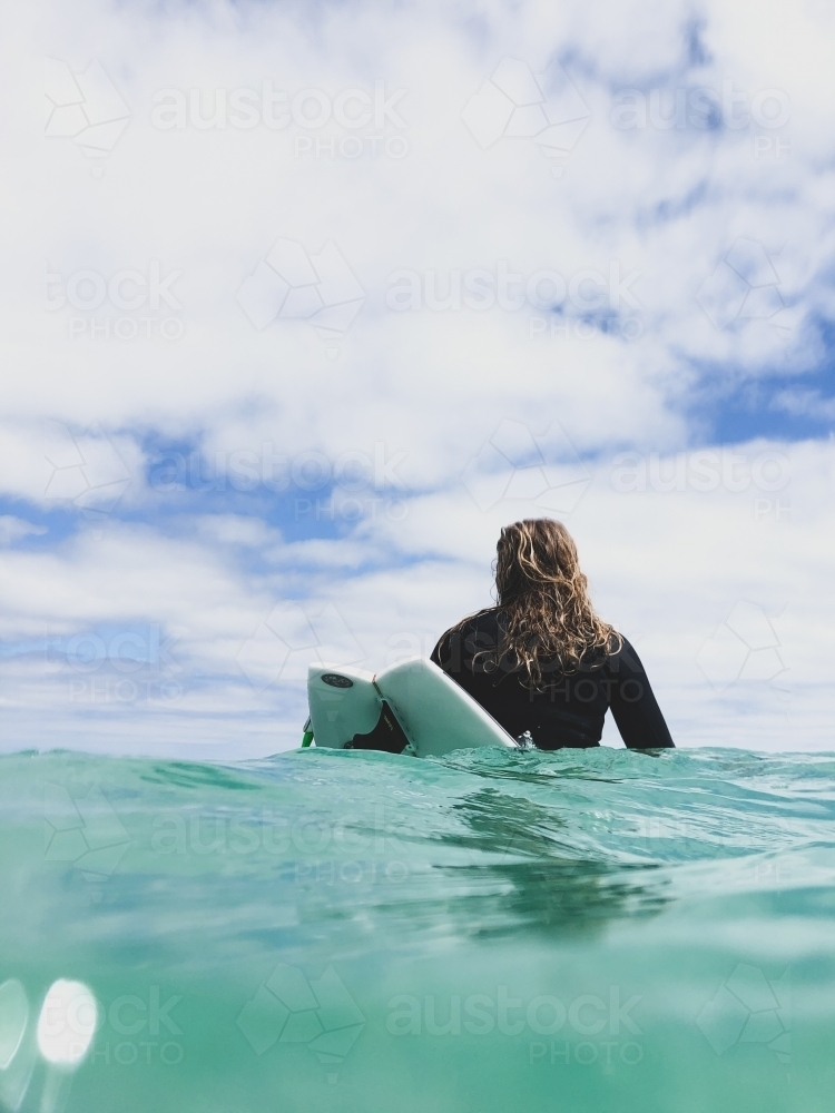 Rear view of Woman sitting on surfboard in ocean - Australian Stock Image