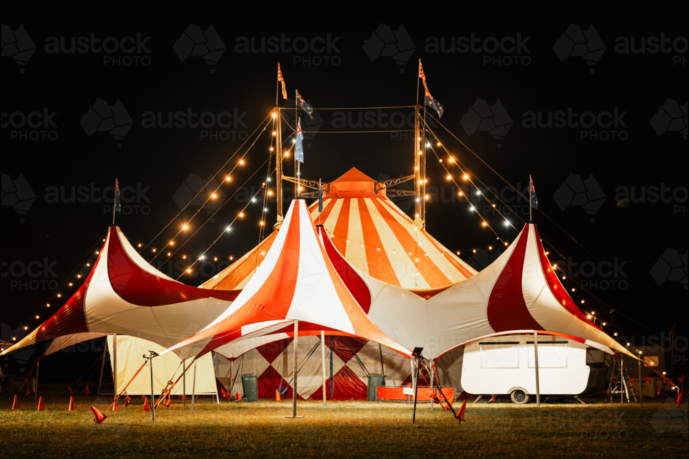 Red and white big top circus tent illuminated at night with Australian flags flying - Australian Stock Image