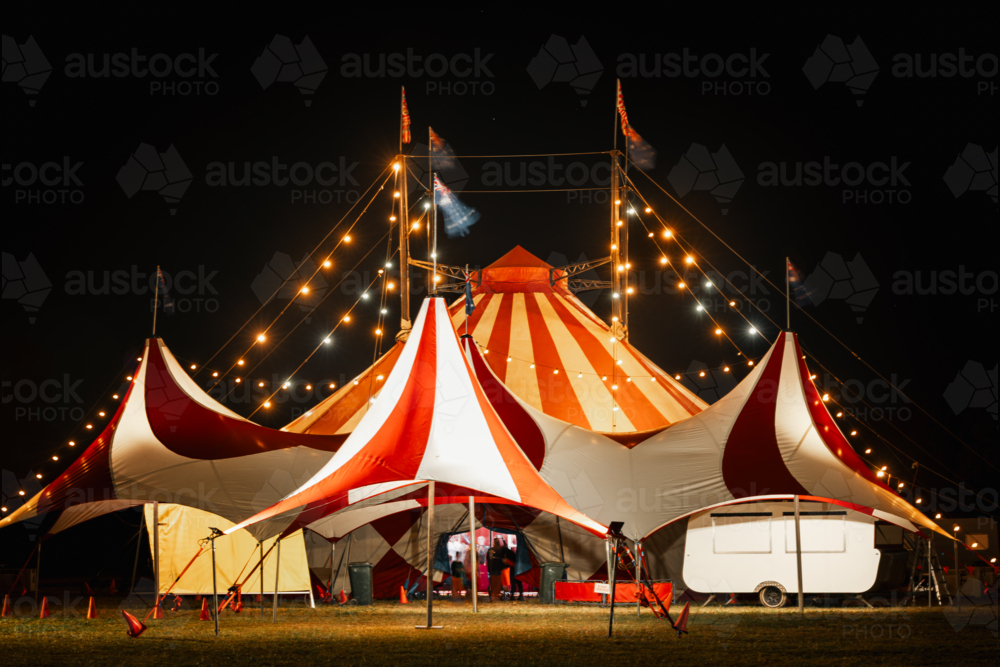 Red and white big top circus tent illuminated at night with people visible through open door - Australian Stock Image