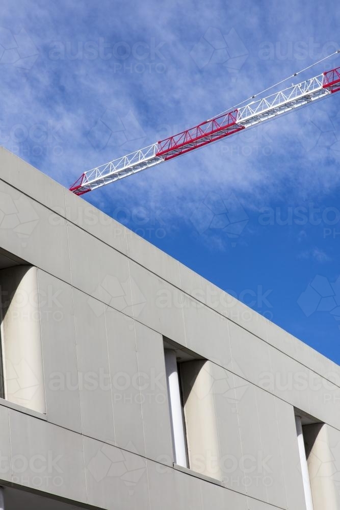 Red and white crane boom near building with cloudy blue sky - Australian Stock Image