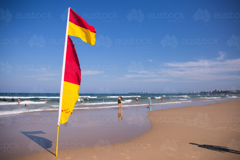 Red and yellow beach safety flags on a sunny summer beach scene with people in water - Australian Stock Image