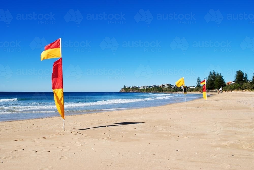 Red and yellow flags at Dicky Beach on a sunny day in winter - Australian Stock Image