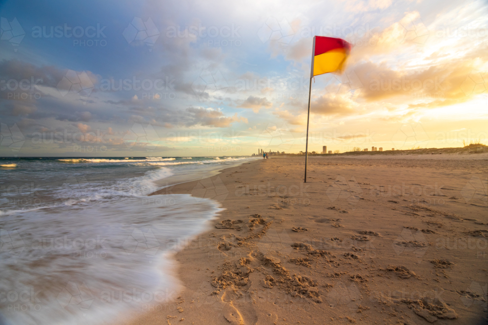 Red and yellow lifeguard flag on sandy beach with waves crashing - Australian Stock Image