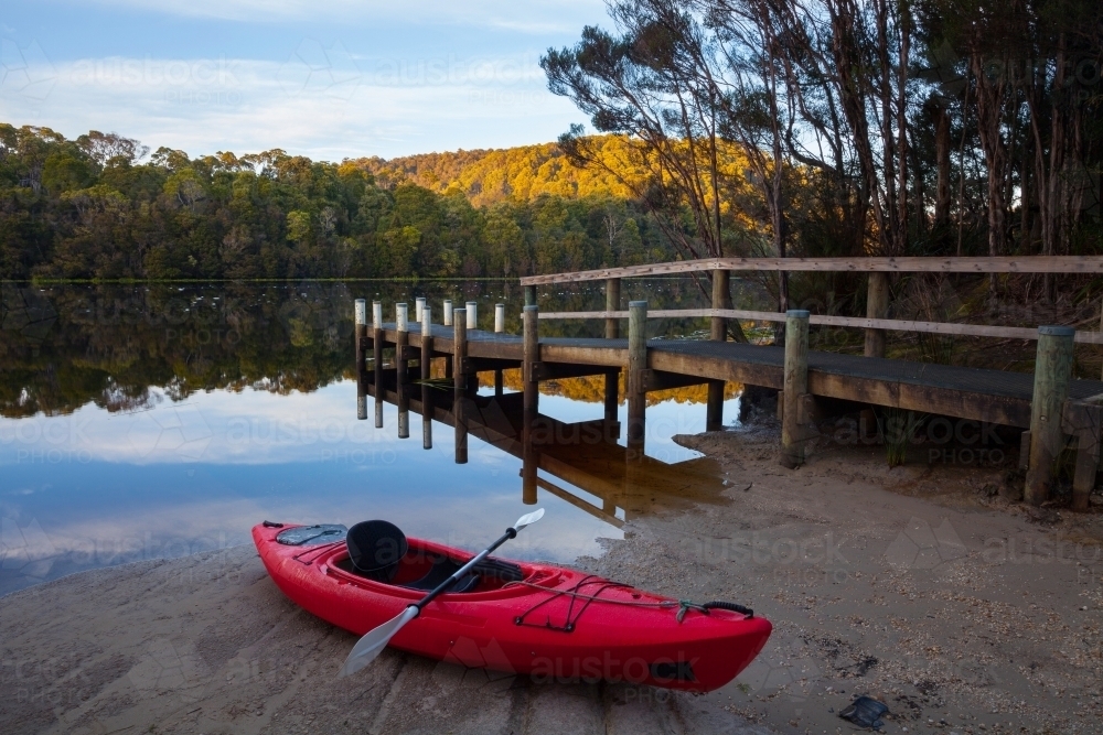Red canoe on sand beside jetty on Pieman River - Australian Stock Image