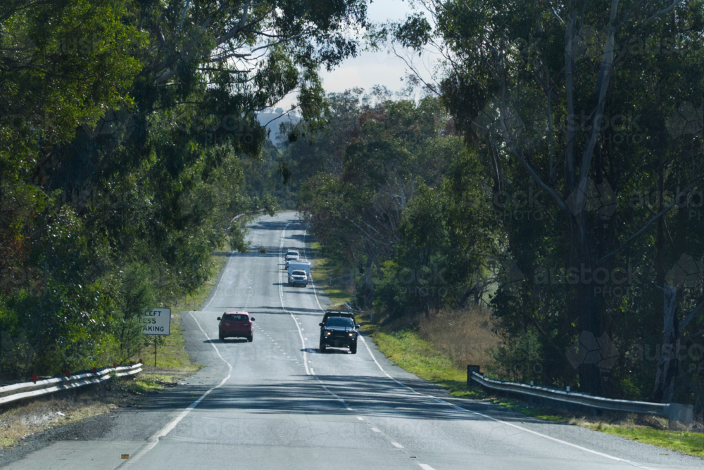 Red car going uphill with cars and caravan going downhill - Australian Stock Image