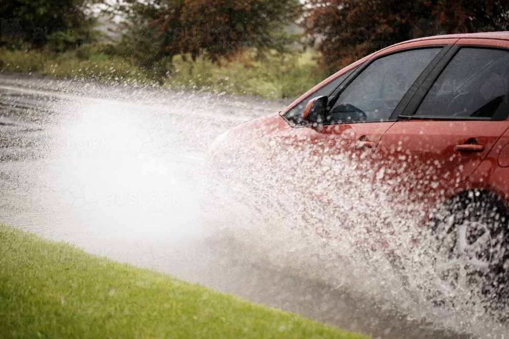 red car on a rainy day driving through a puddle creating a big splash - Australian Stock Image