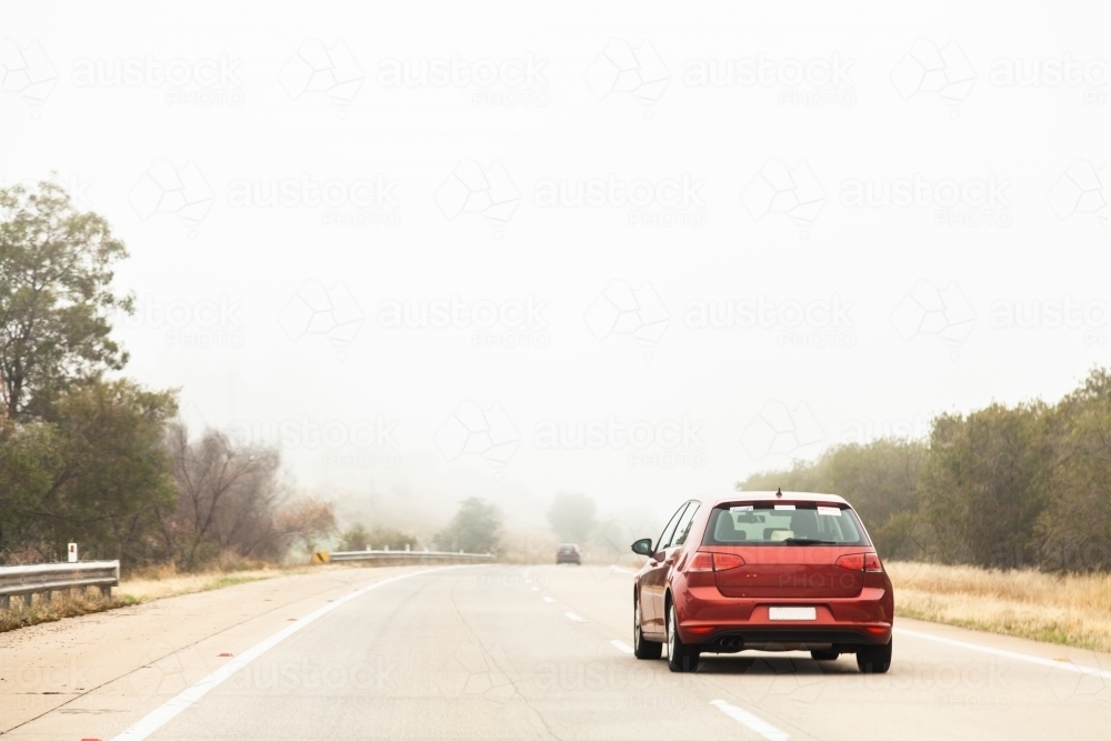 Red car overtaking in the right hand lane in foggy conditions - Australian Stock Image