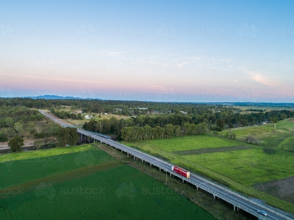 Red cattle truck on bridge travelling through green farmland in country - Australian Stock Image