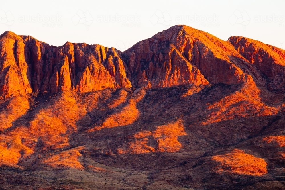 Red coloured cliffs and jagged edges of Mount Sonder early in the morning. - Australian Stock Image