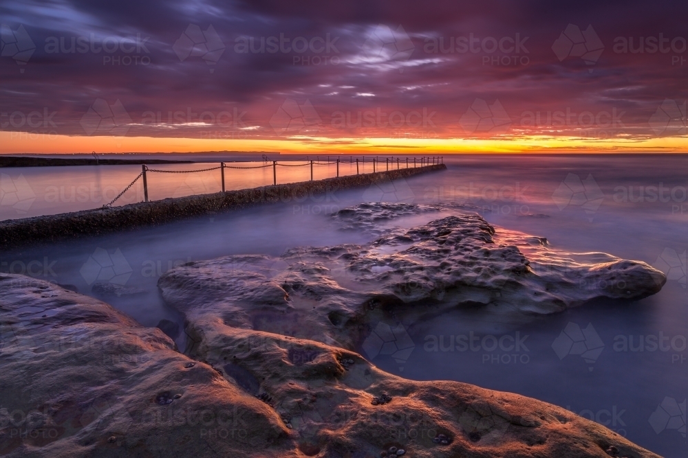 Red dawn skies at Oak Park Ocean Pool Cronulla - Australian Stock Image
