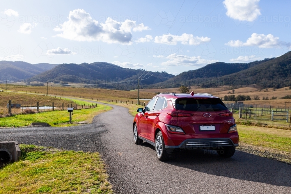 Image of Red electric vehicle car driving down rural country road in