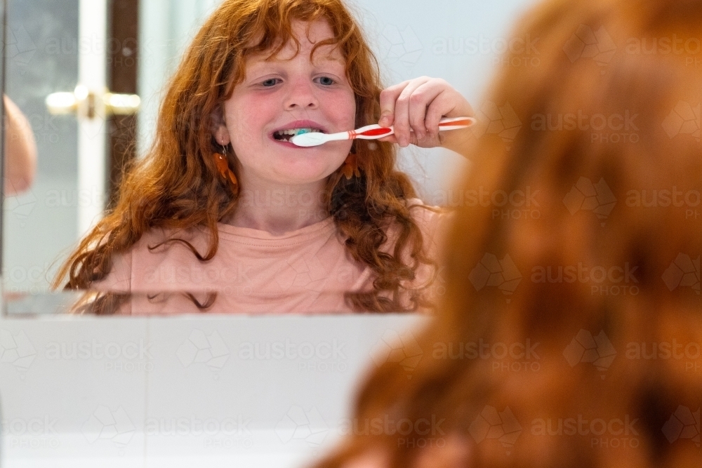 red-haired child reflected in bathroom mirror cleaning teeth - Australian Stock Image
