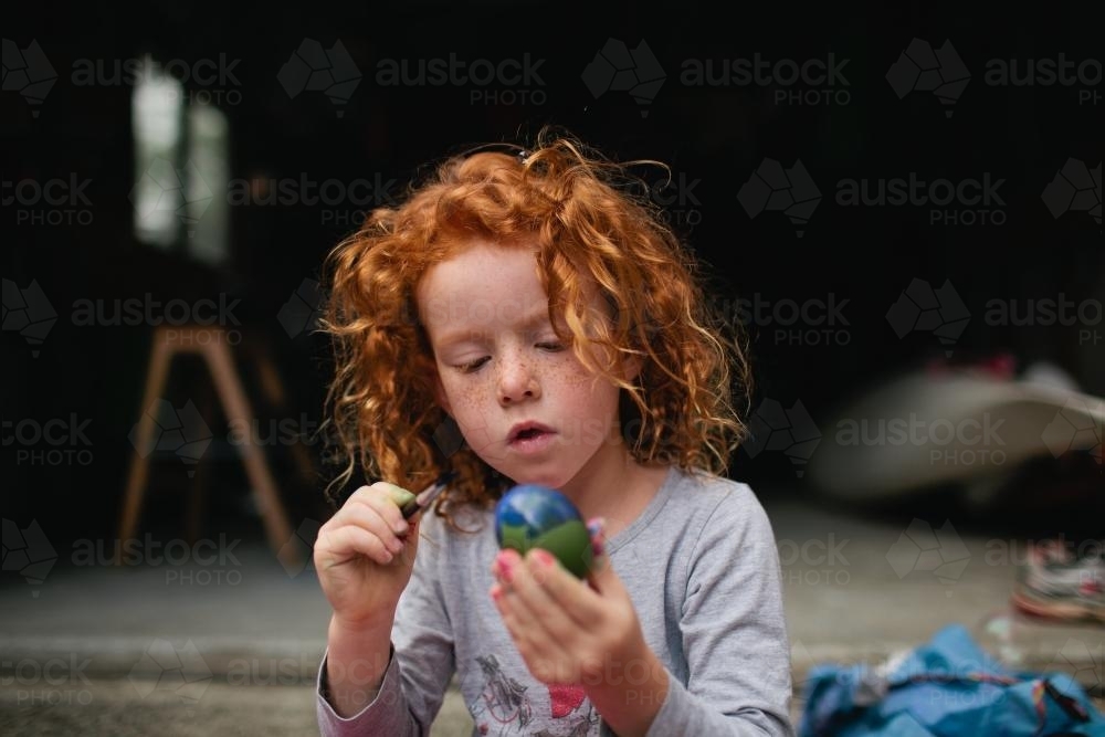 Red haired girl painting easter eggs - Australian Stock Image