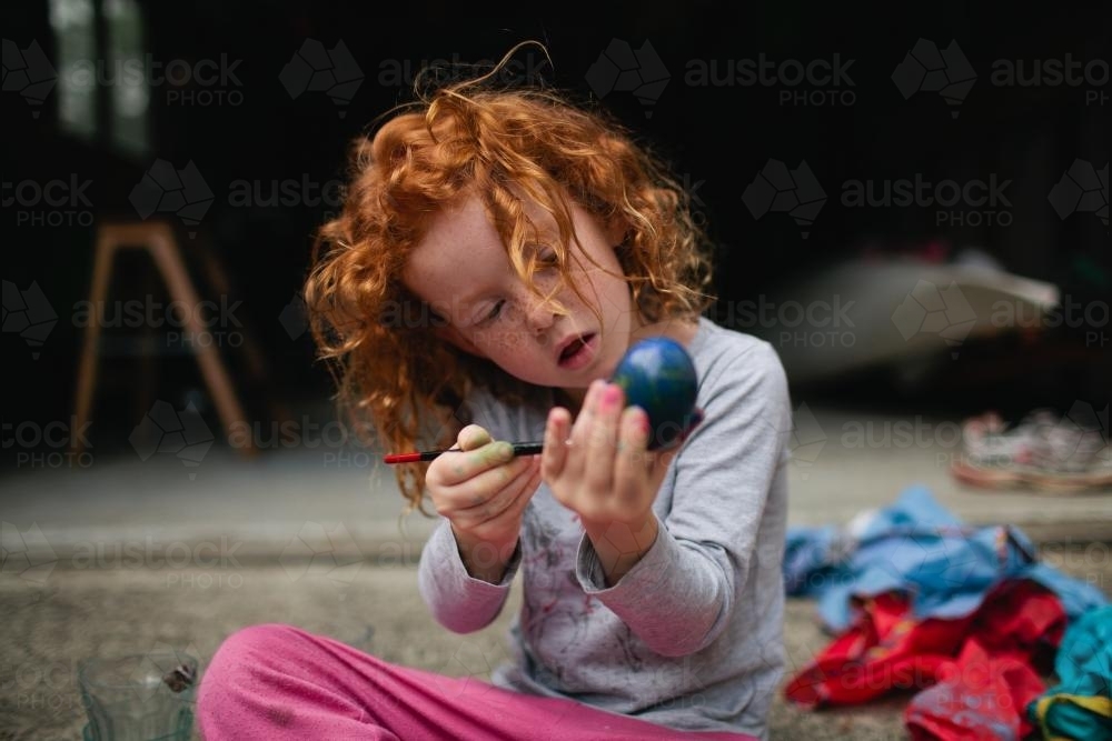 Red haired girl painting easter eggs - Australian Stock Image