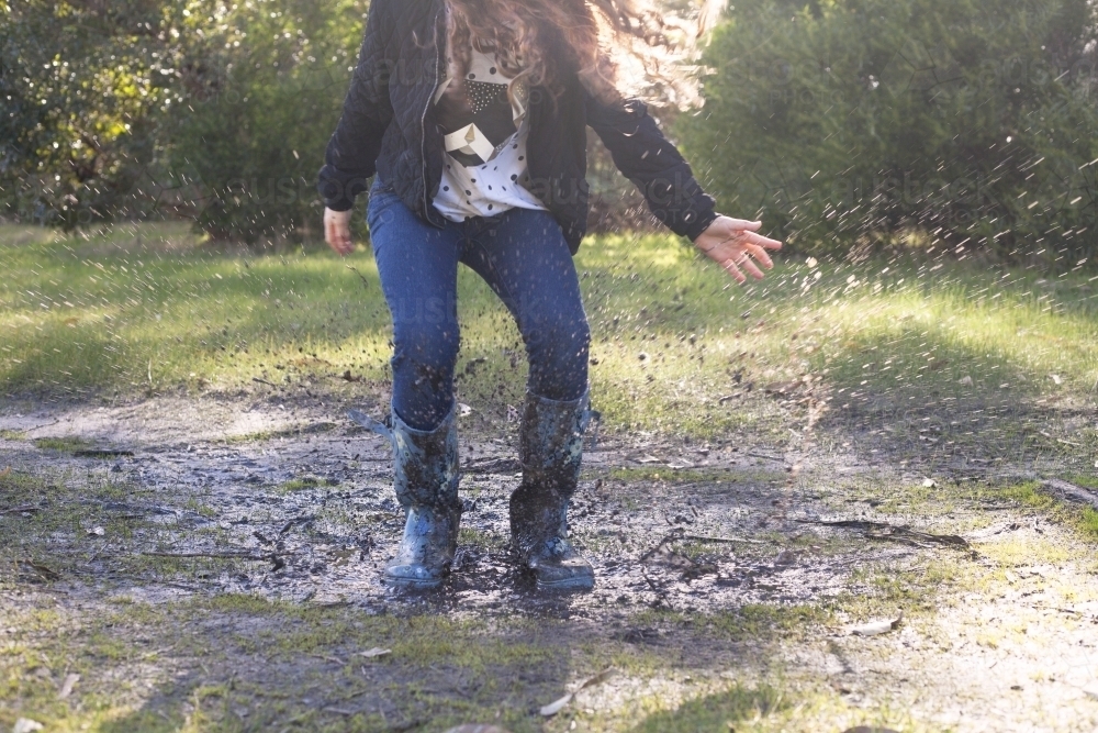 Red haired girl splashing in puddles in gumboots on a rainy winter day. - Australian Stock Image