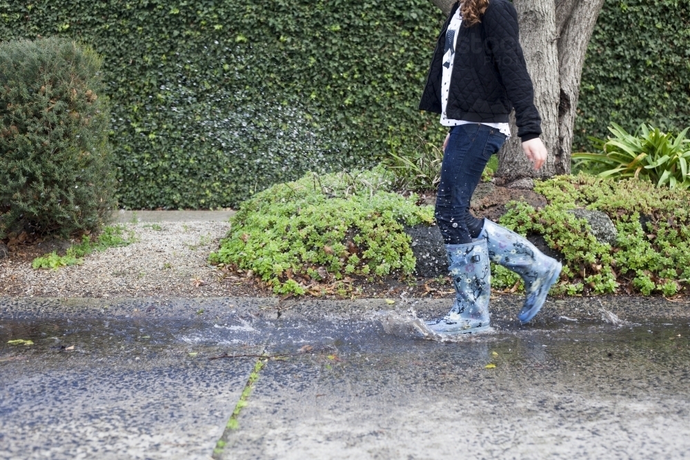 Red haired girl splashing in puddles in gumboots on a rainy winter day. - Australian Stock Image