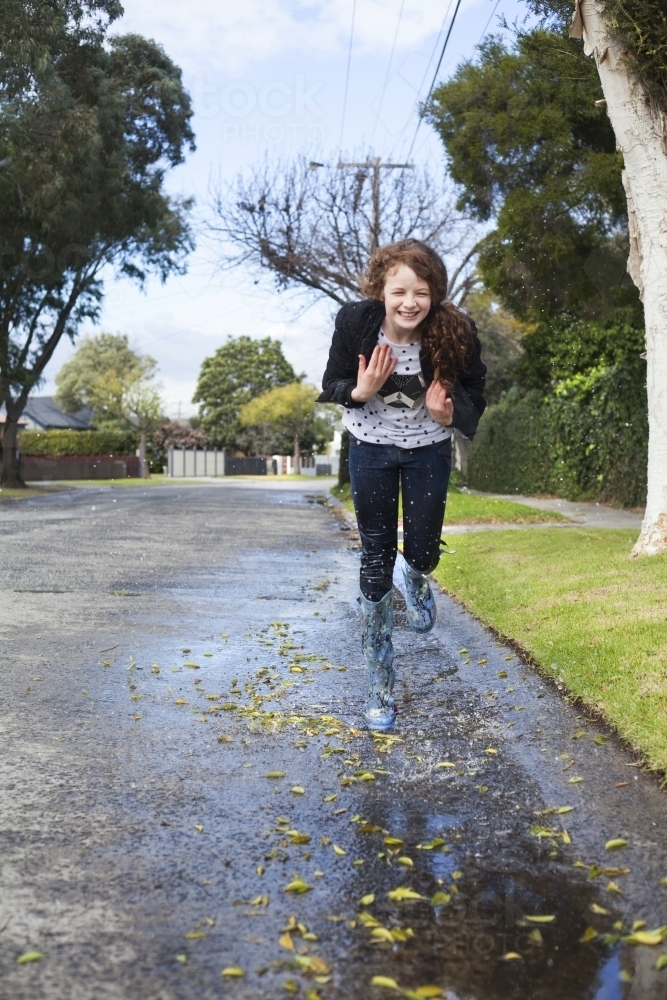 Red haired girl splashing in puddles in gumboots on a rainy winter day. - Australian Stock Image