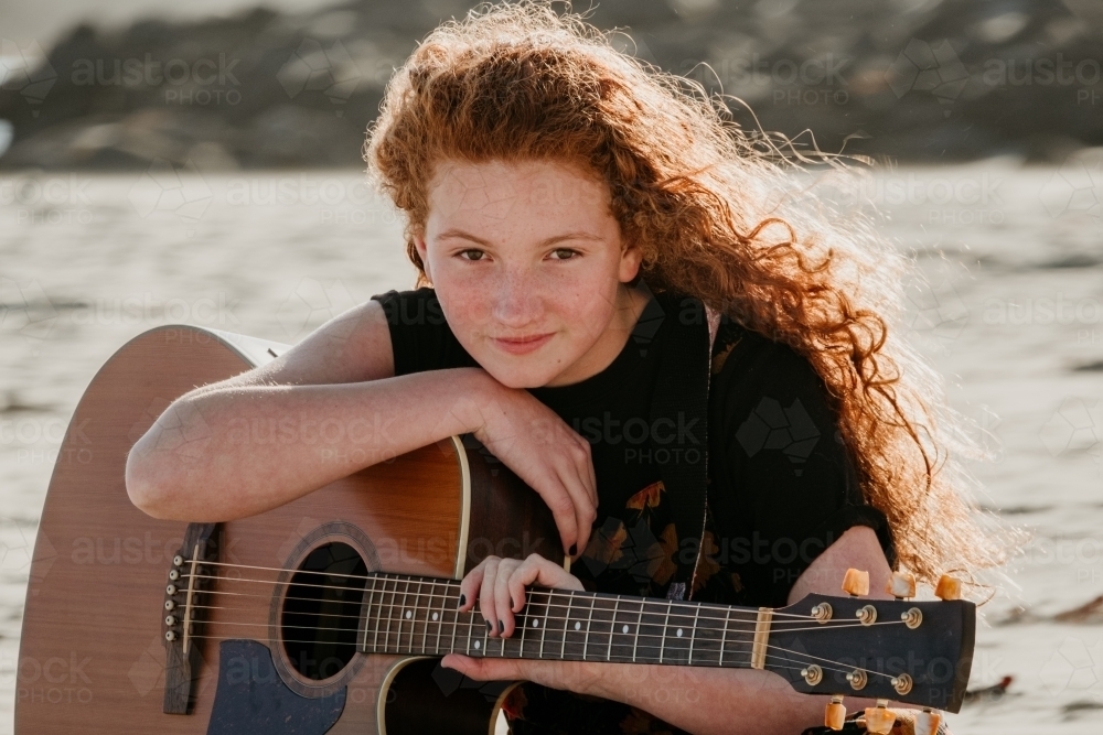 Red haired teen sitting with her guitar on the beach. - Australian Stock Image