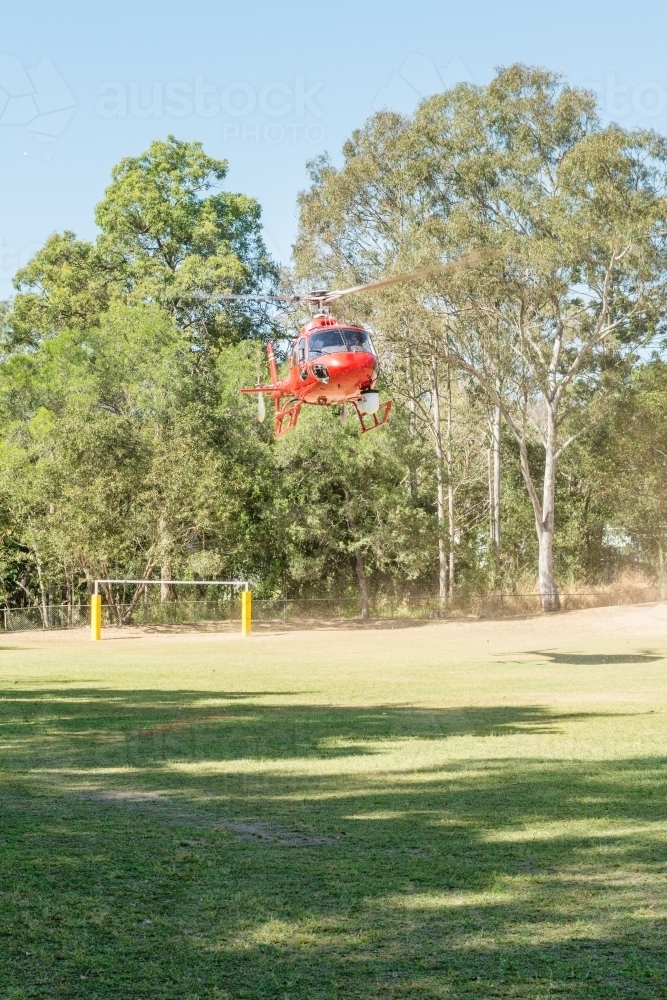 Red helicopter landing on a school oval - Australian Stock Image