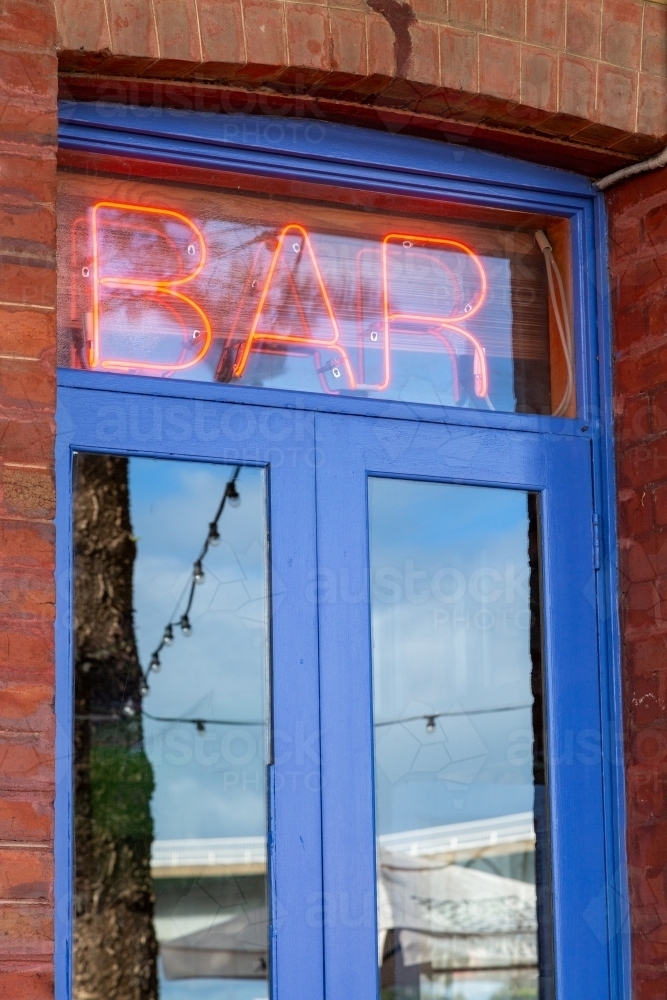 Red neon bar sign above blue door and brick building. - Australian Stock Image