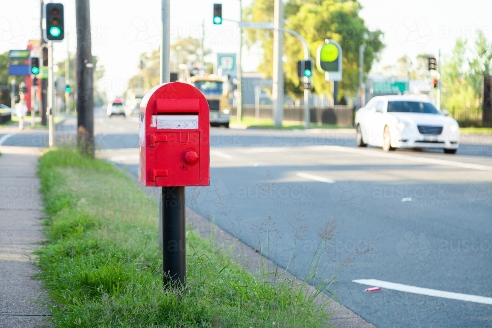 Red post box for mail next to a footpath beside the road - Australian Stock Image