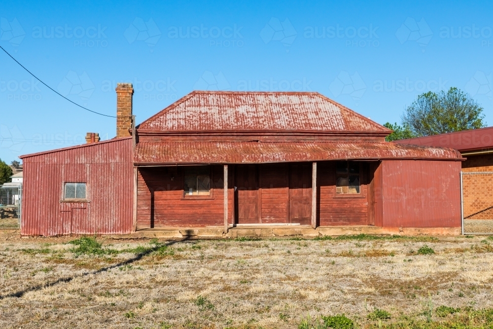Red rusted, sun drenched, rundown, country house against a clear blue sky - Australian Stock Image
