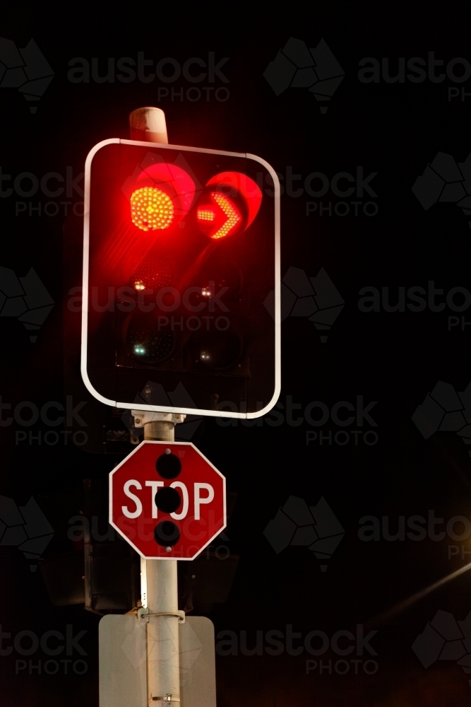 Red stop sign at intersection with traffic lights at night time - Australian Stock Image