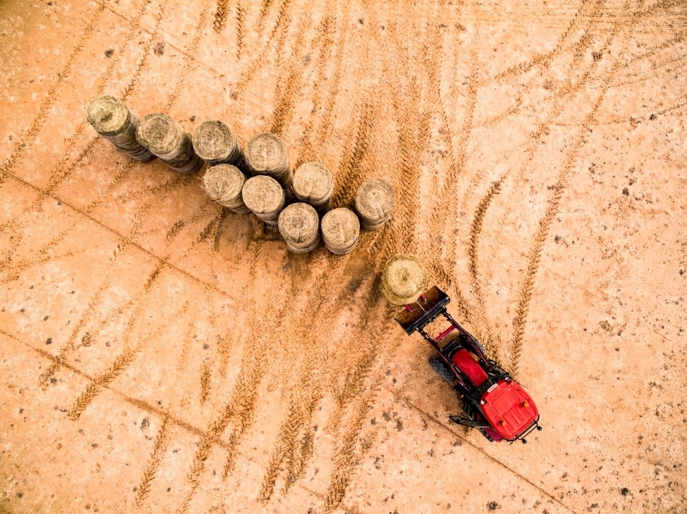 Red tractor moving  large hay bales. - Australian Stock Image