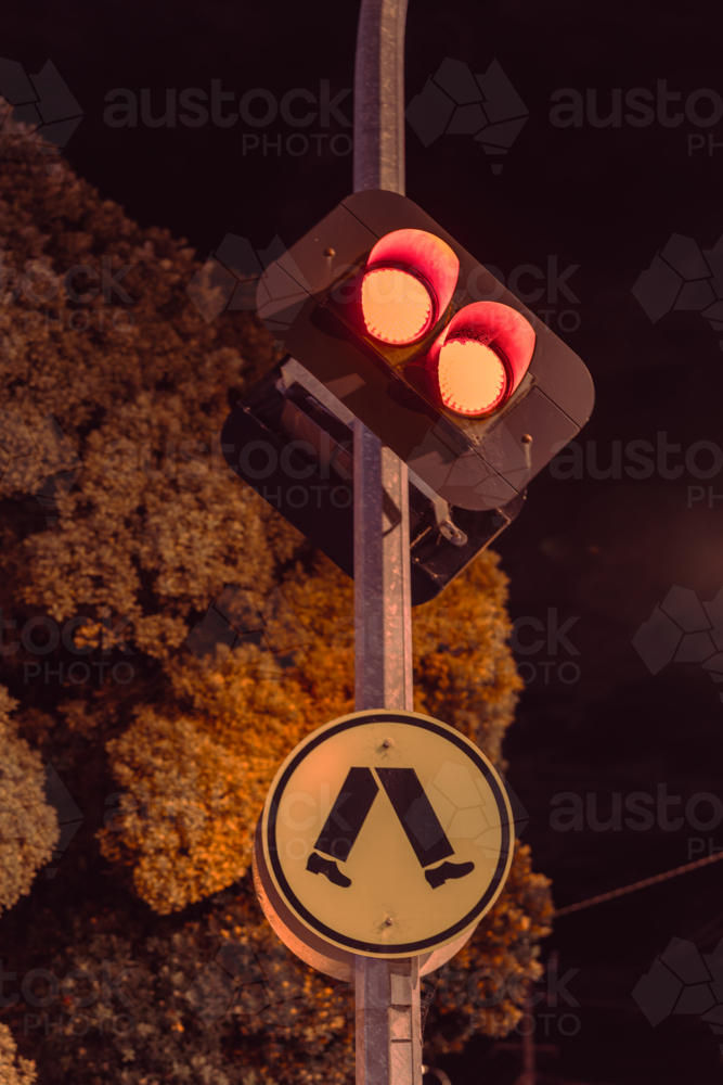 Red traffic light with pedestrian crossing sign at night - Australian Stock Image