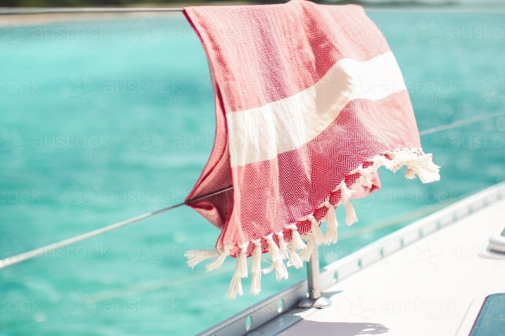 Red turkish towel hanging on wire railing of boat on the water - Australian Stock Image