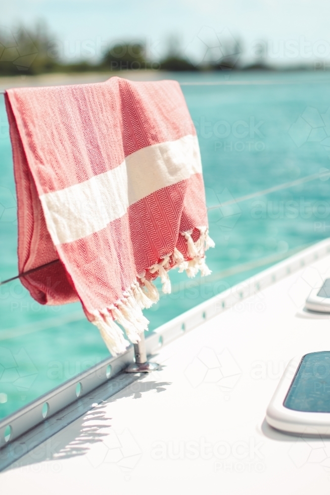 Red turkish towel hanging on wire railing of boat on the water - Australian Stock Image