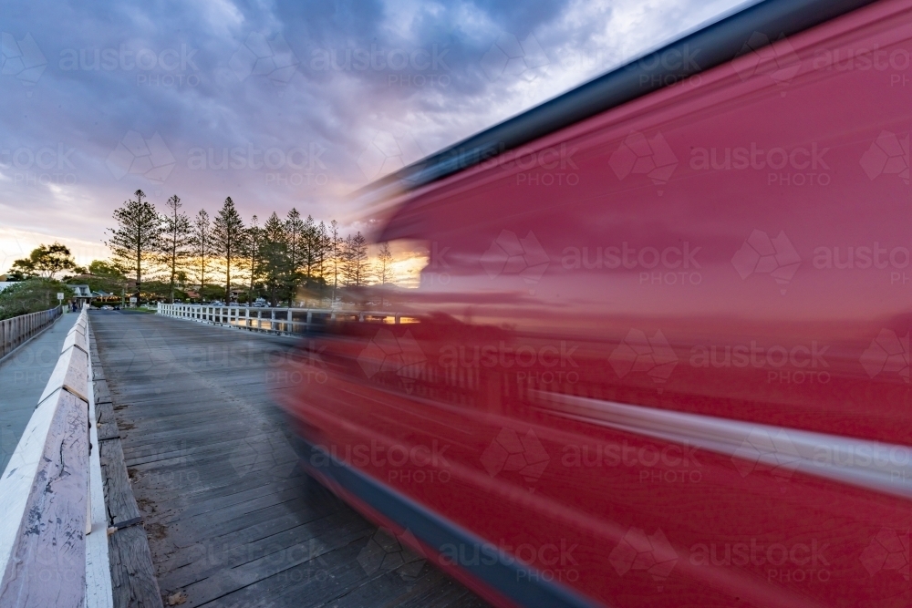 Red van with motion blur crossing bridge at sunset - Australian Stock Image