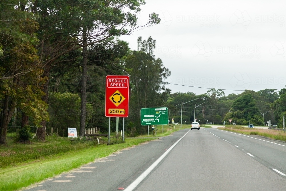 Reduce speed sign before a roundabout on highway - Australian Stock Image
